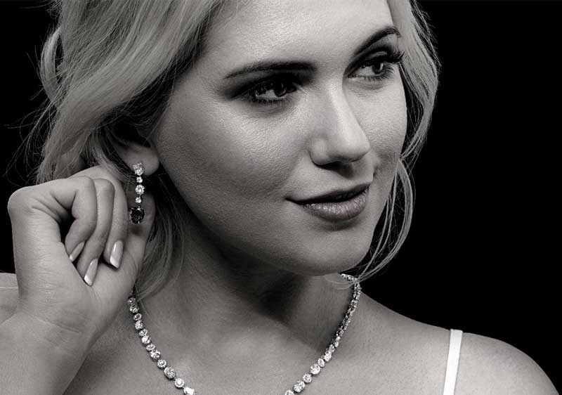 Grayscale image of a woman wearing diamond earrings and a diamond necklace.