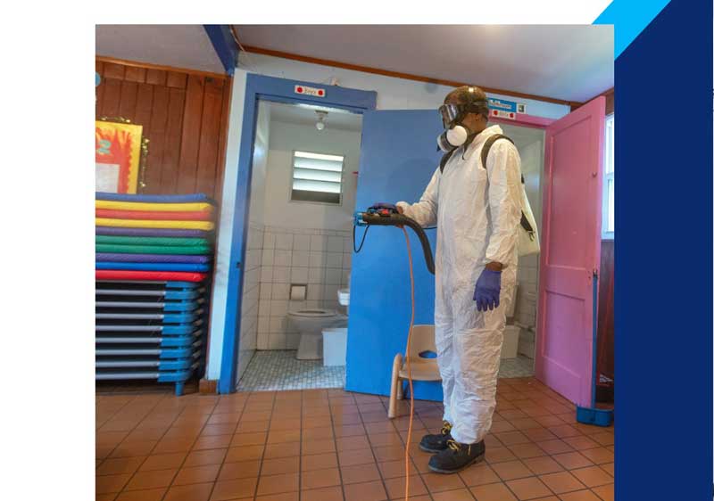 Man in a protective suit with a mask, conducting pest inspection and spraying in a bathroom