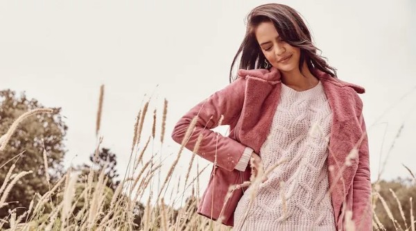 A beautiful woman wearing a pink jacket standing in a field