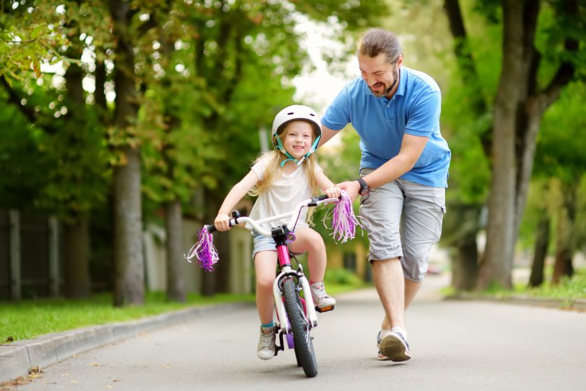 Happy father helping daughter with bike training