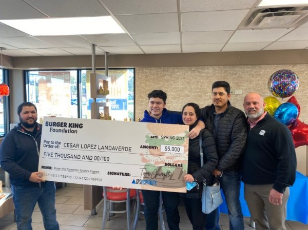 A man holding a large cardboard check with his family by his side, celebrating their achievement