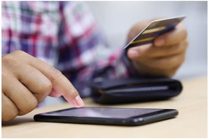 Person using a phone and holding a credit card in the other hand